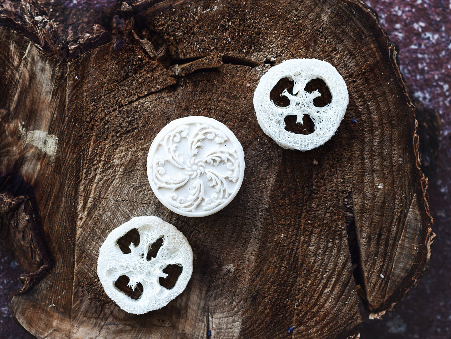 picture of reduce soap with pinwheel design, surrounded by loofah discs on a cedar tree round
