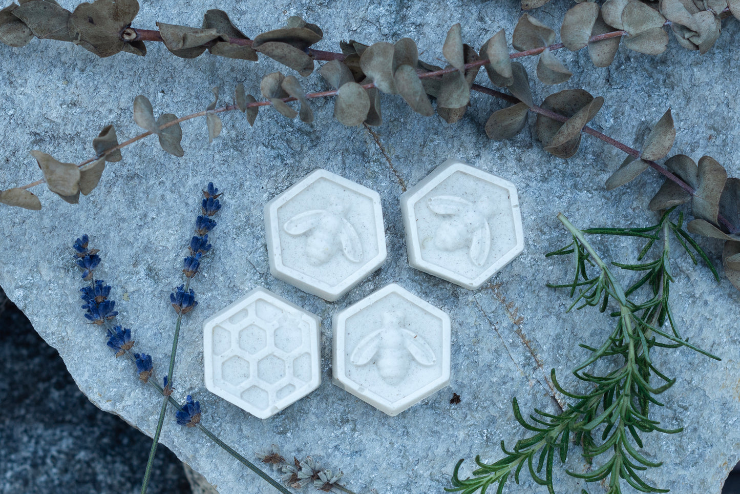 picture of 4 honey comb shaped soothe variety soaps on a slate slab, surrounded by fresh rosemary, lavender, and eucalyptus