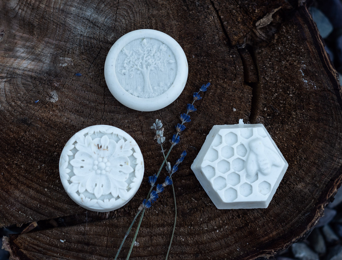 picture of three calm variety soaps with lavender flowers all sitting on a cedar tree round. soap designs are the tree, the flower, and the large honeycomb