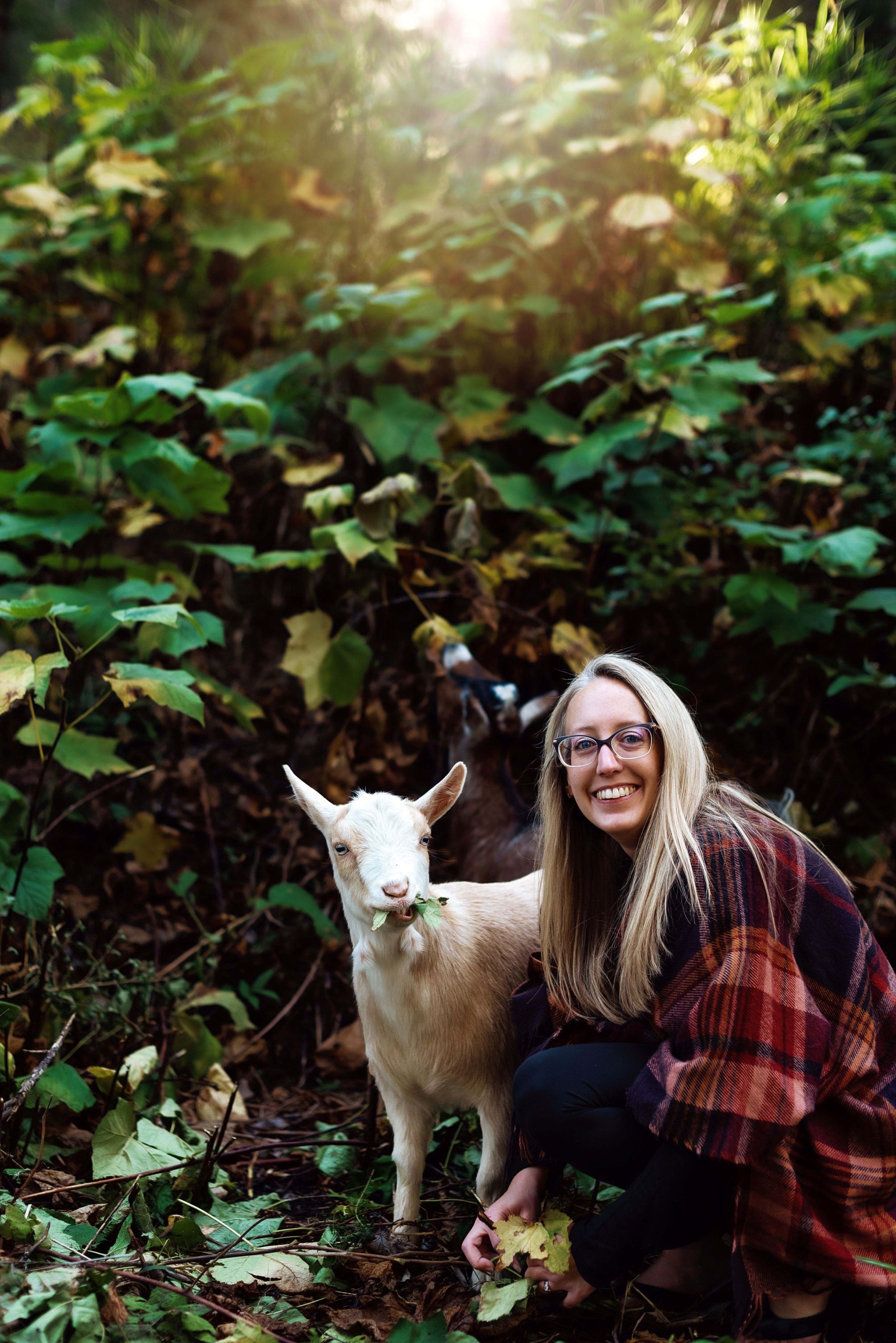 Picture of me and my goat who is eating leaves in front of a foliage backdrop